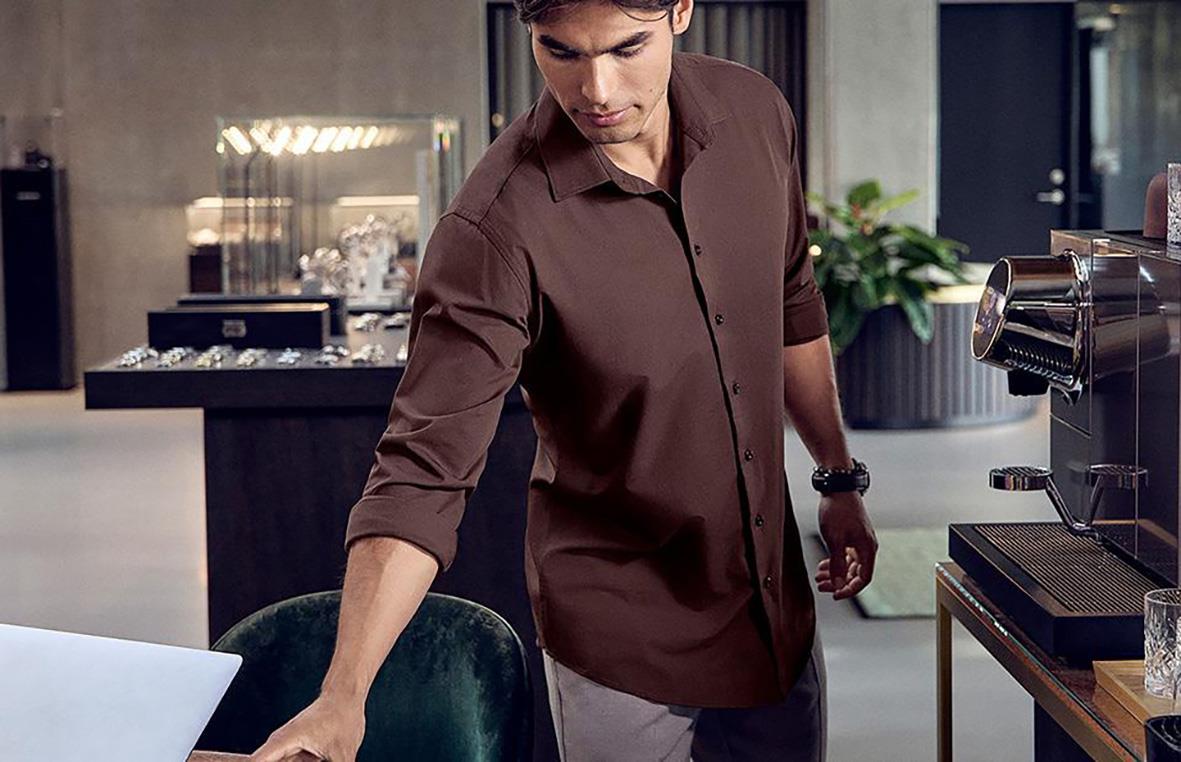 Man i brunt skjorta i ett modernt kontorsmiljö, står vid ett bord med laptop