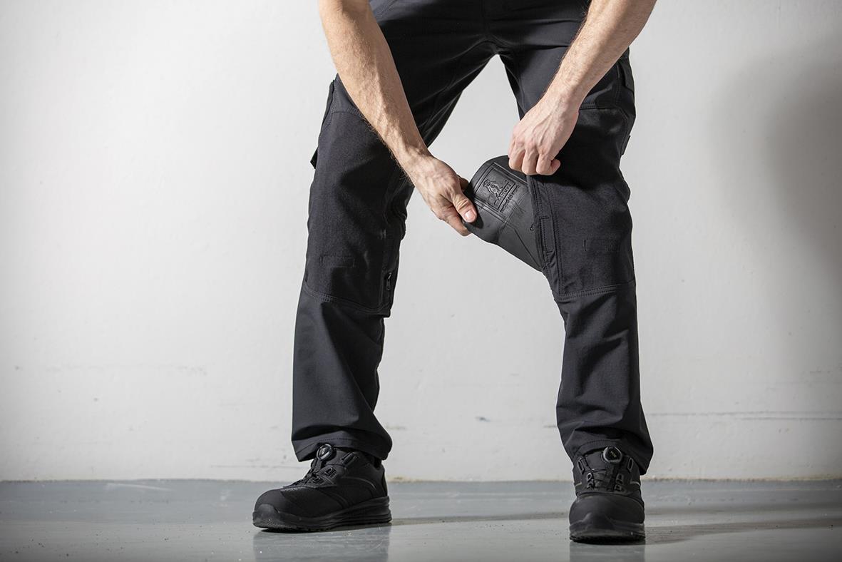 Person som bär grå knäskydd och svarta byxor, står mot en ljus bakgrund