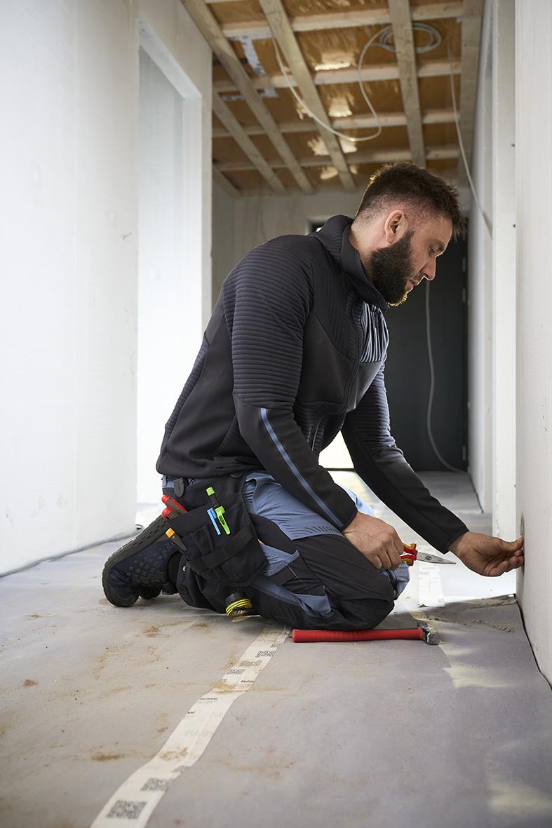 Elektriker i mörk marin hängficka arbetar på byggarbetsplats, installerar eller kontrollerar ledningar