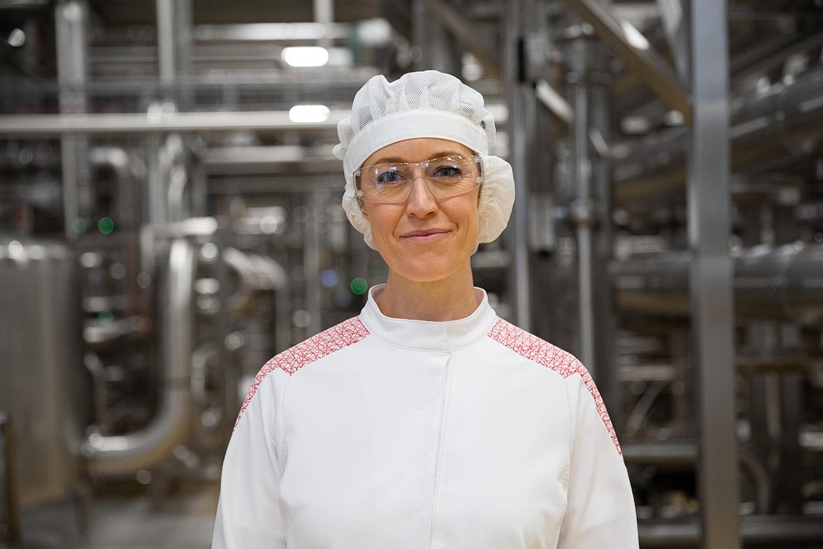 Kvinna i vit arbetsdräkt och skyddsglasögon i industrimiljö