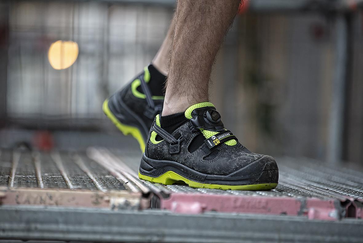 Skyddssko Arbesko 929 i svart med gröna detaljer, person står på en metallbänk