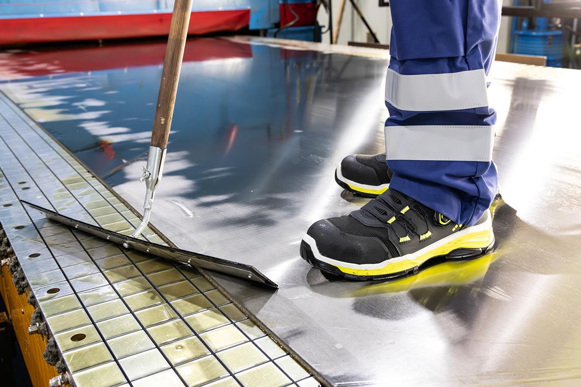 Person i skyddsskor Jalas TIO 2058 Svart/Gul står på metallgolv i industriell miljö