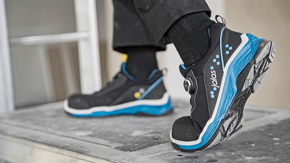 Svarta och blå skyddsskor Jalas TIO 2028 på en person stående på en träbänk