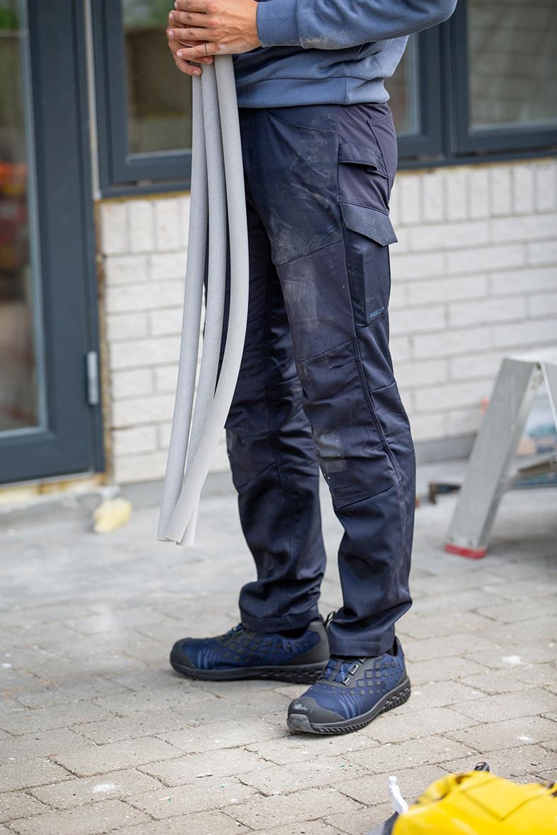 Person står utomhus i arbetskläder, bär skyddsskor och håller långa vita slangar