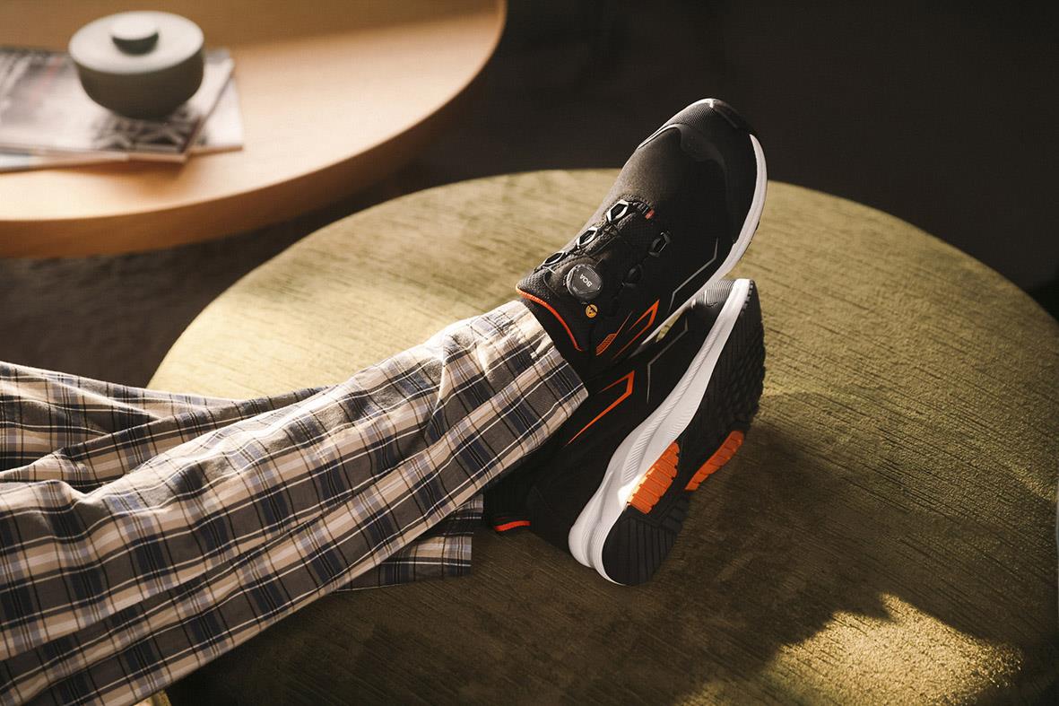 Person som vilar fötterna på en stol, visar en svart skyddssko med orange detaljer