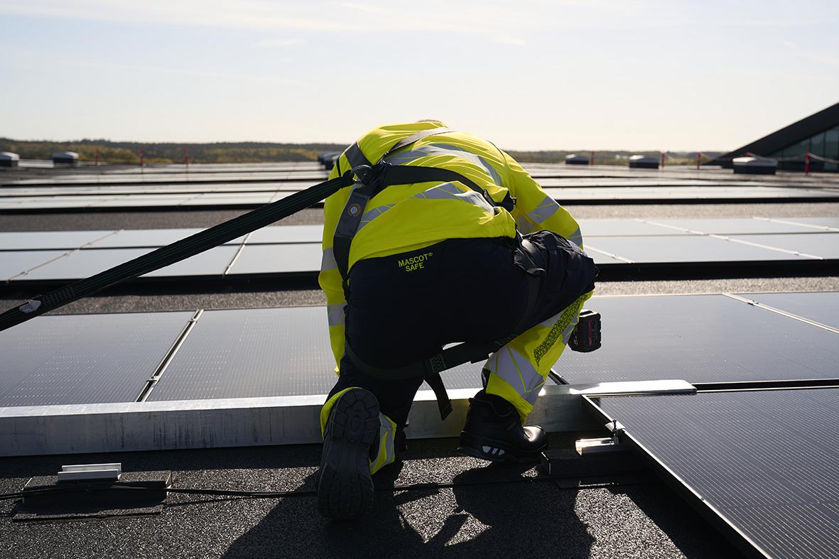 Person installerar solpaneler på taket, bär skyddssko och reflexväst