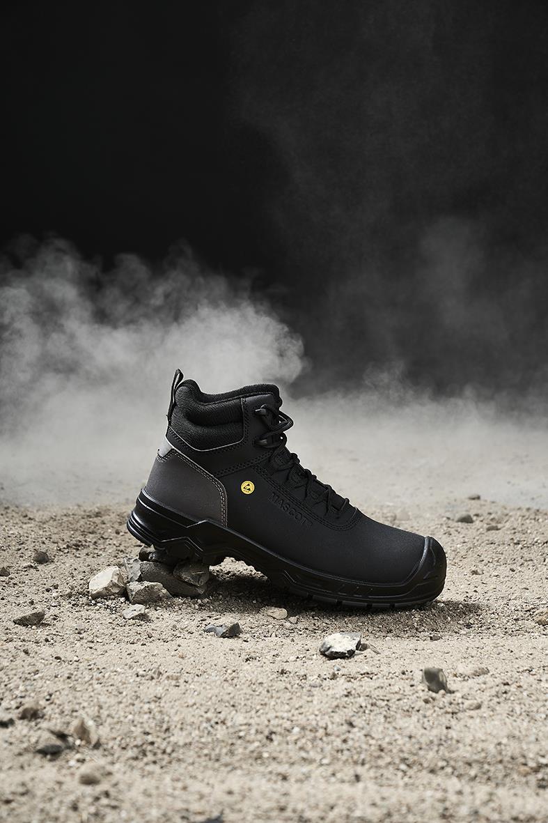 Svart skyddskänga Mascot F1007-906-09 S3S på grusig mark med damm eller ånga i bakgrunden