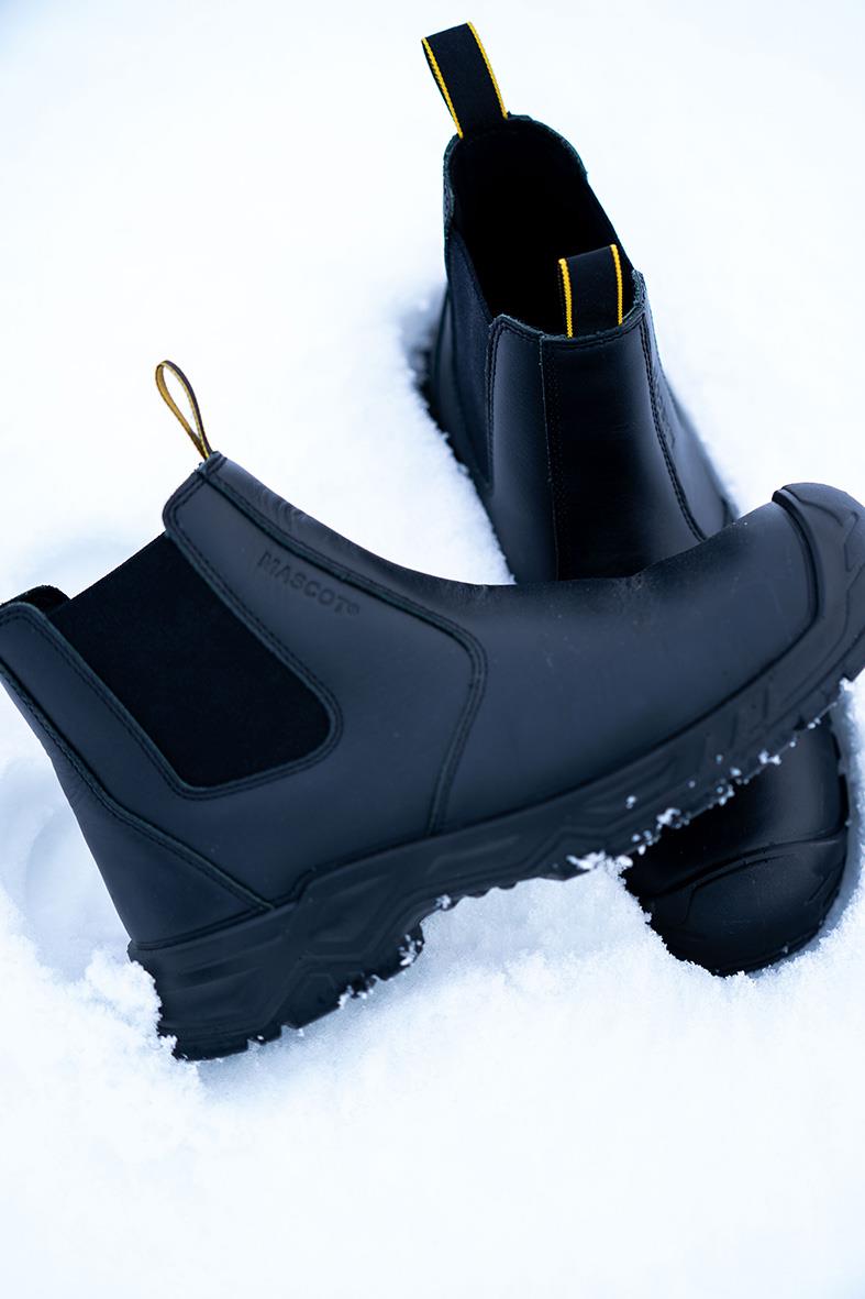 Svarta skyddskängor i gummi med tjock sula och dragöglor, placerade i snö