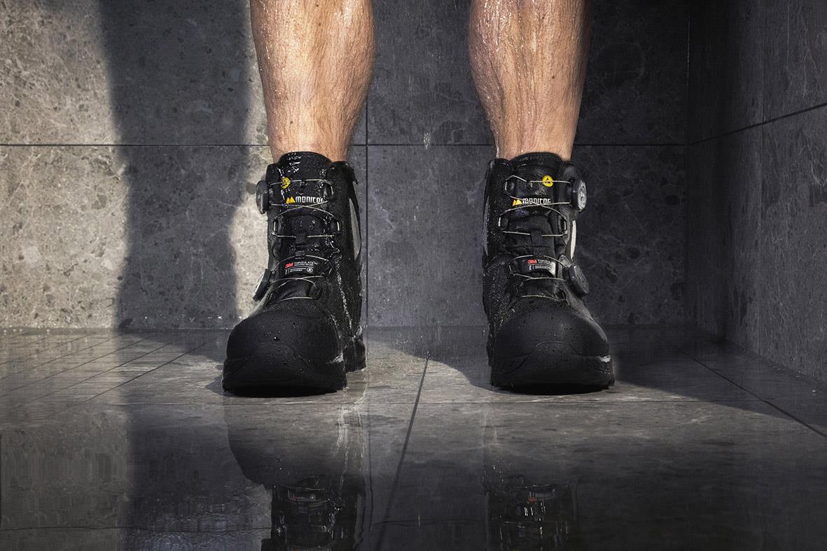 Skyddskänga Monitor Arctic Mid 44 på en persons fötter, svart med guldetaljer