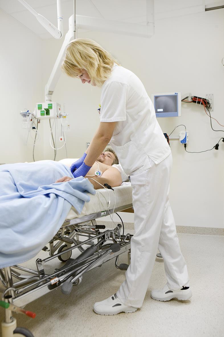 Sjuksköterska undersöker patient i sjukhusvård, vit klädsel, medicinsk utrustning i bakgrunden