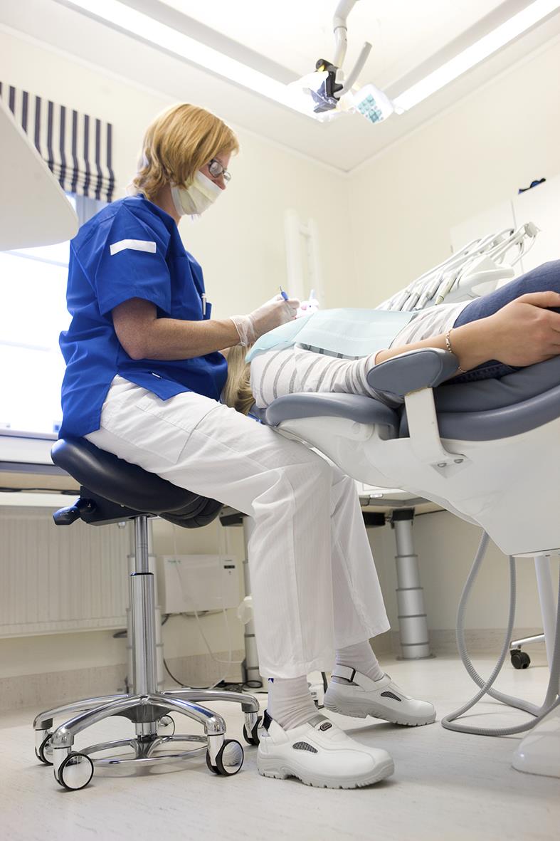 Sjuksköterska i blå arbetskläder och ansiktsmask vid patient i sjukhusmiljö