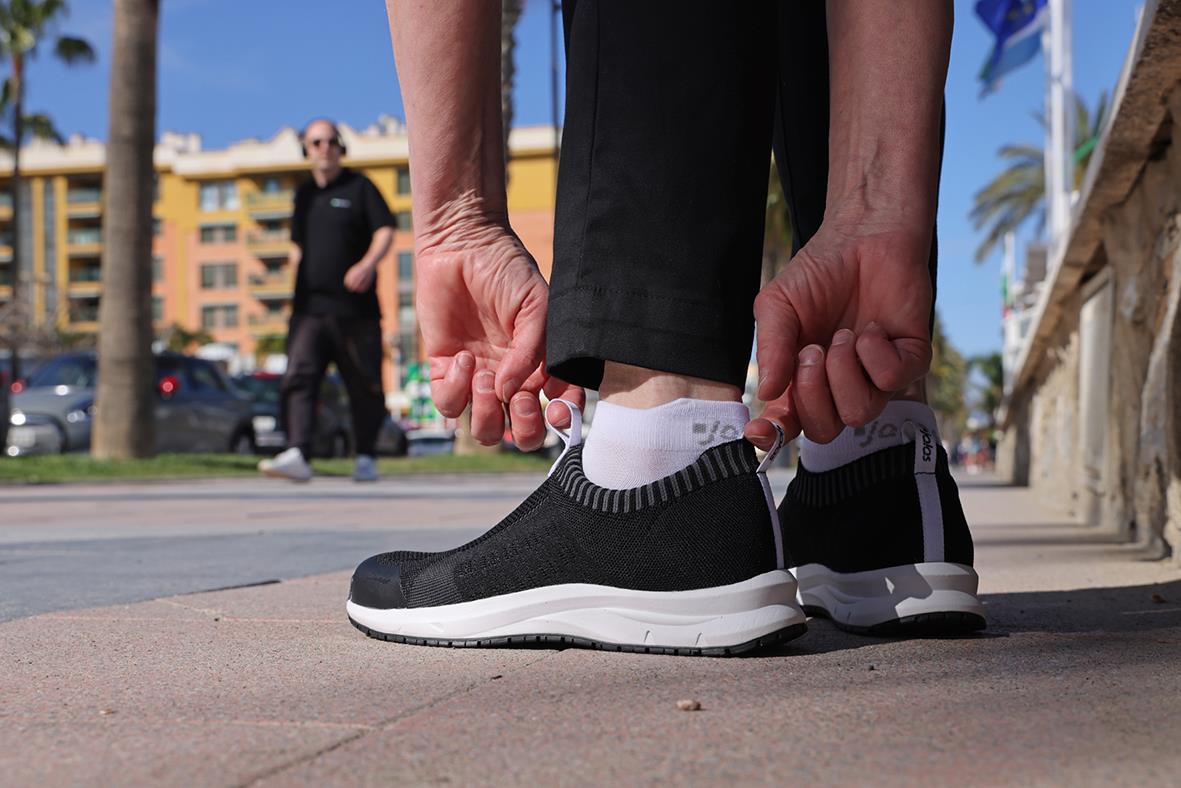 Person som knäpper på sig svarta och vita arbets- eller sportskor utomhus