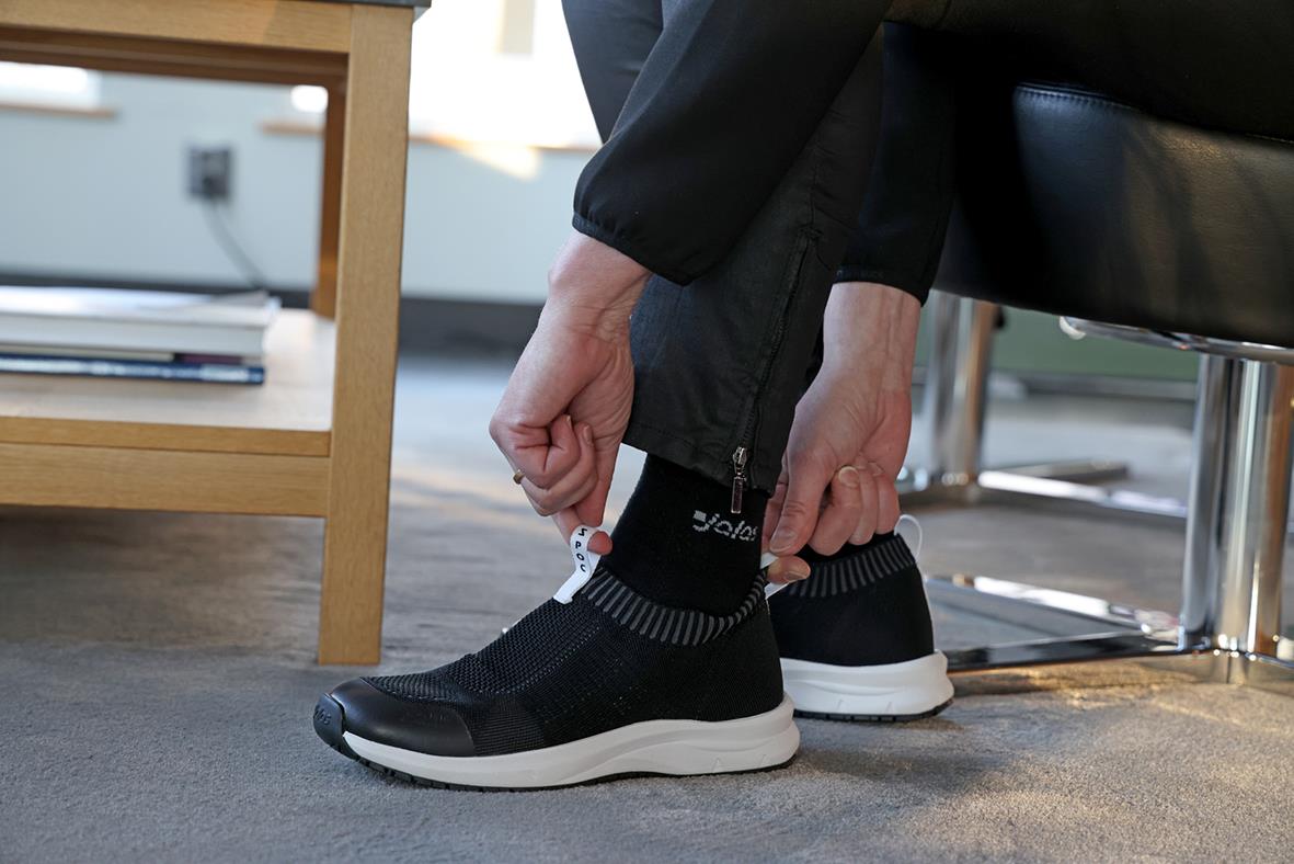 Person som sätter på sig svarta arbets- eller sportskor i ett kontorsliknande miljö