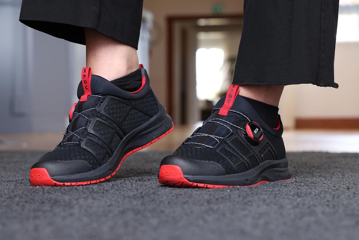 Svarta arbetsskor med röda detaljer och BOA-spänne, visade på en person i svarta byxor