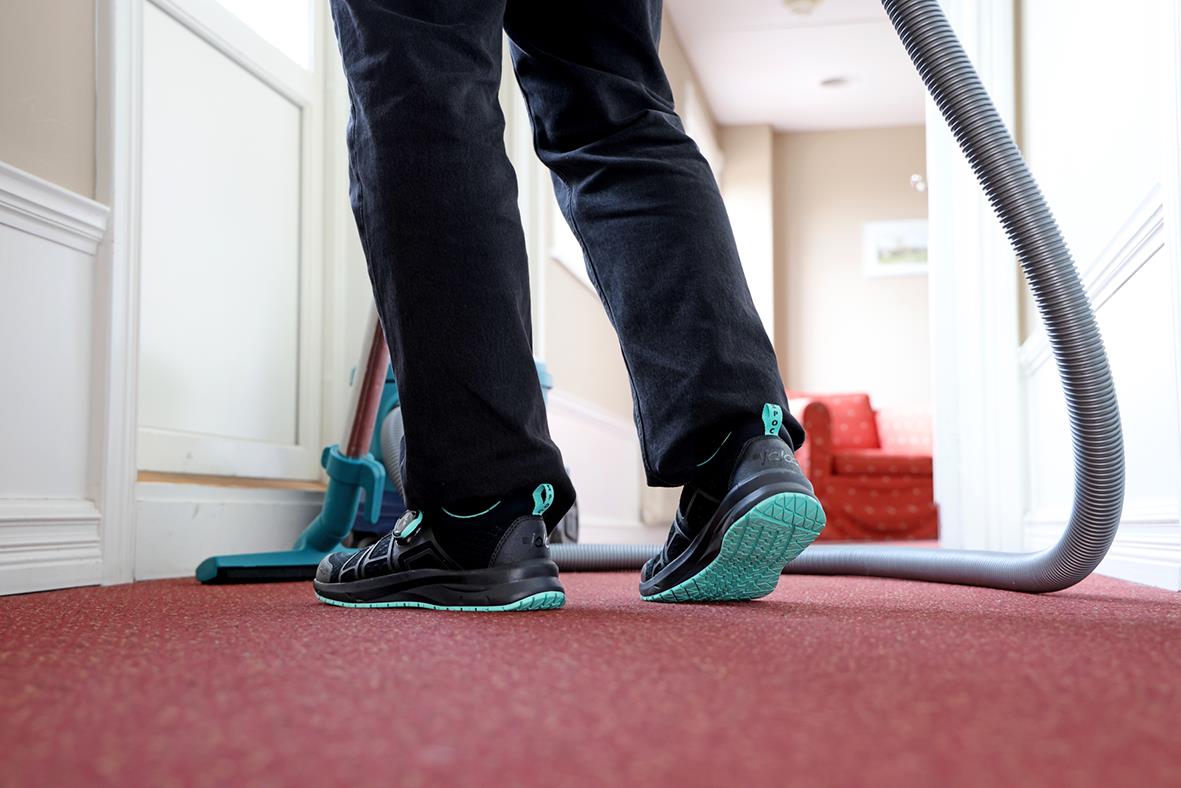 Person som använder en blå och svart dammsugare på en röd matta inomhus