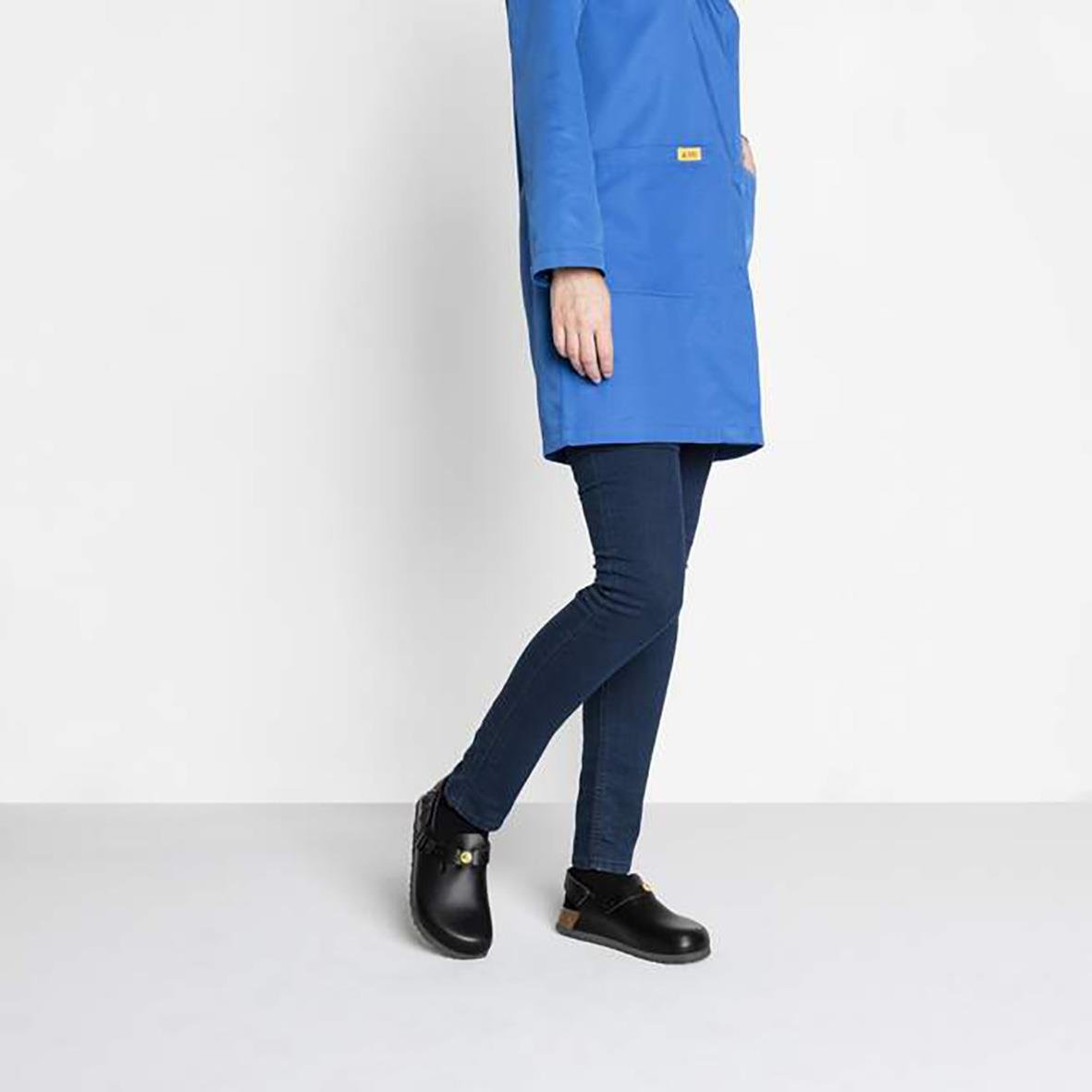 Person i blå jacka och svarta Birkenstock Tokio ESD sandaler mot en ljus bakgrund