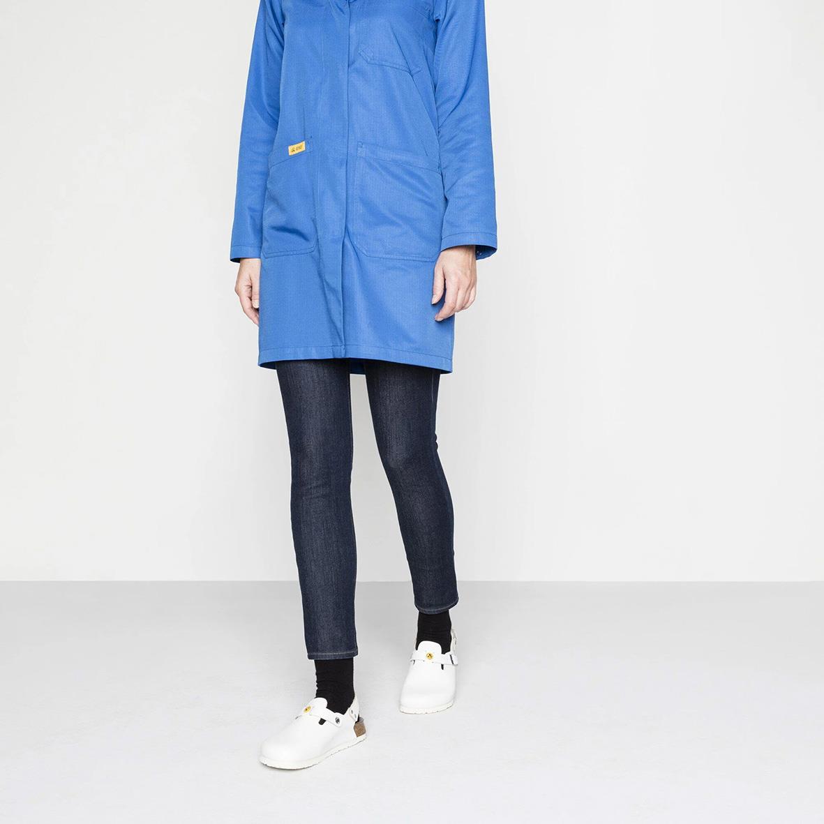 Person i blå jacka, mörka jeans och vita sneakers står mot vit bakgrund