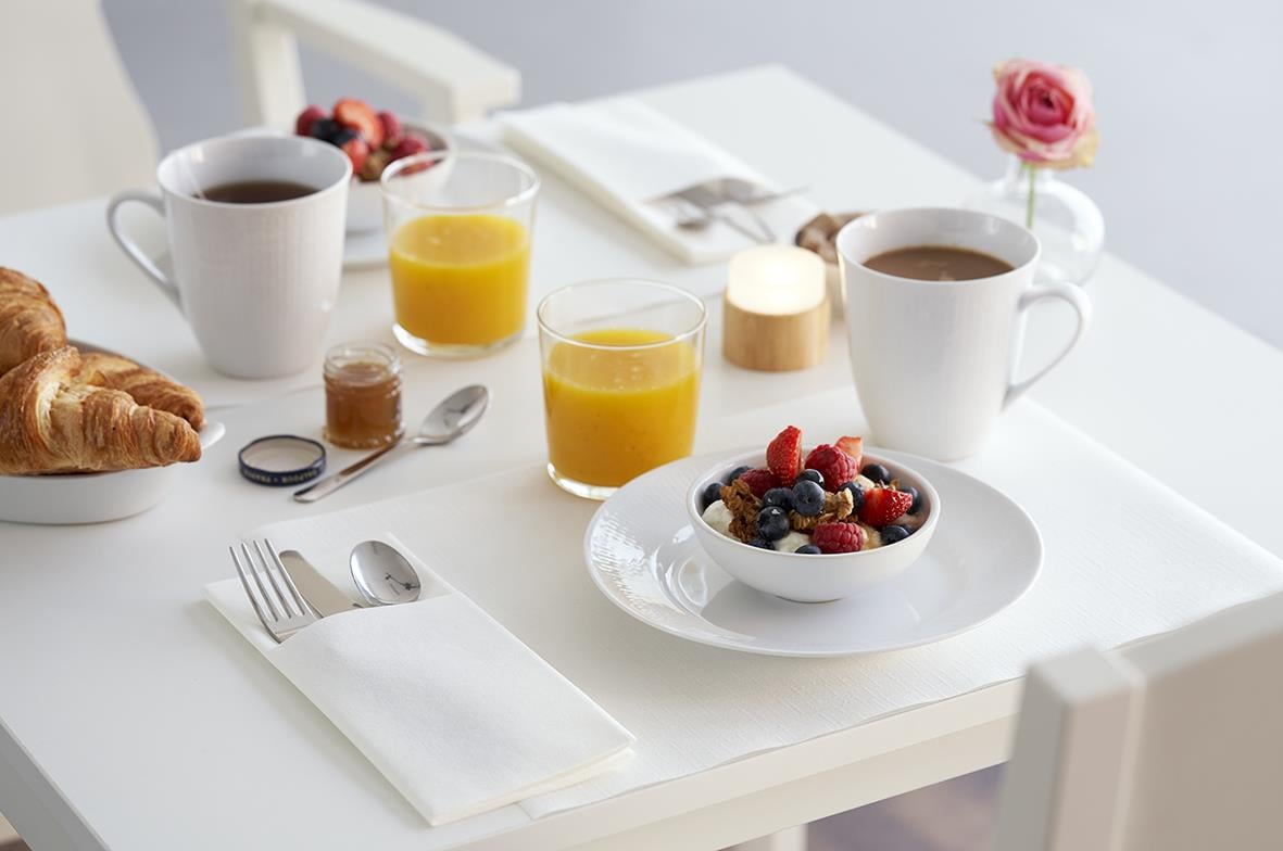 Frukostbord med ljus, kaffe, juice, croissant och frukt