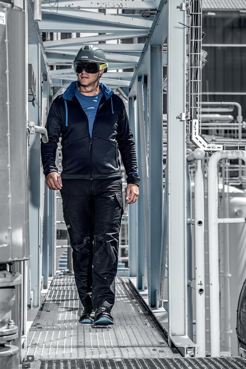 Man i industrimiljö med gråa korgglasögon Uvex Megasonic 93202, mörk klädsel och hjälm