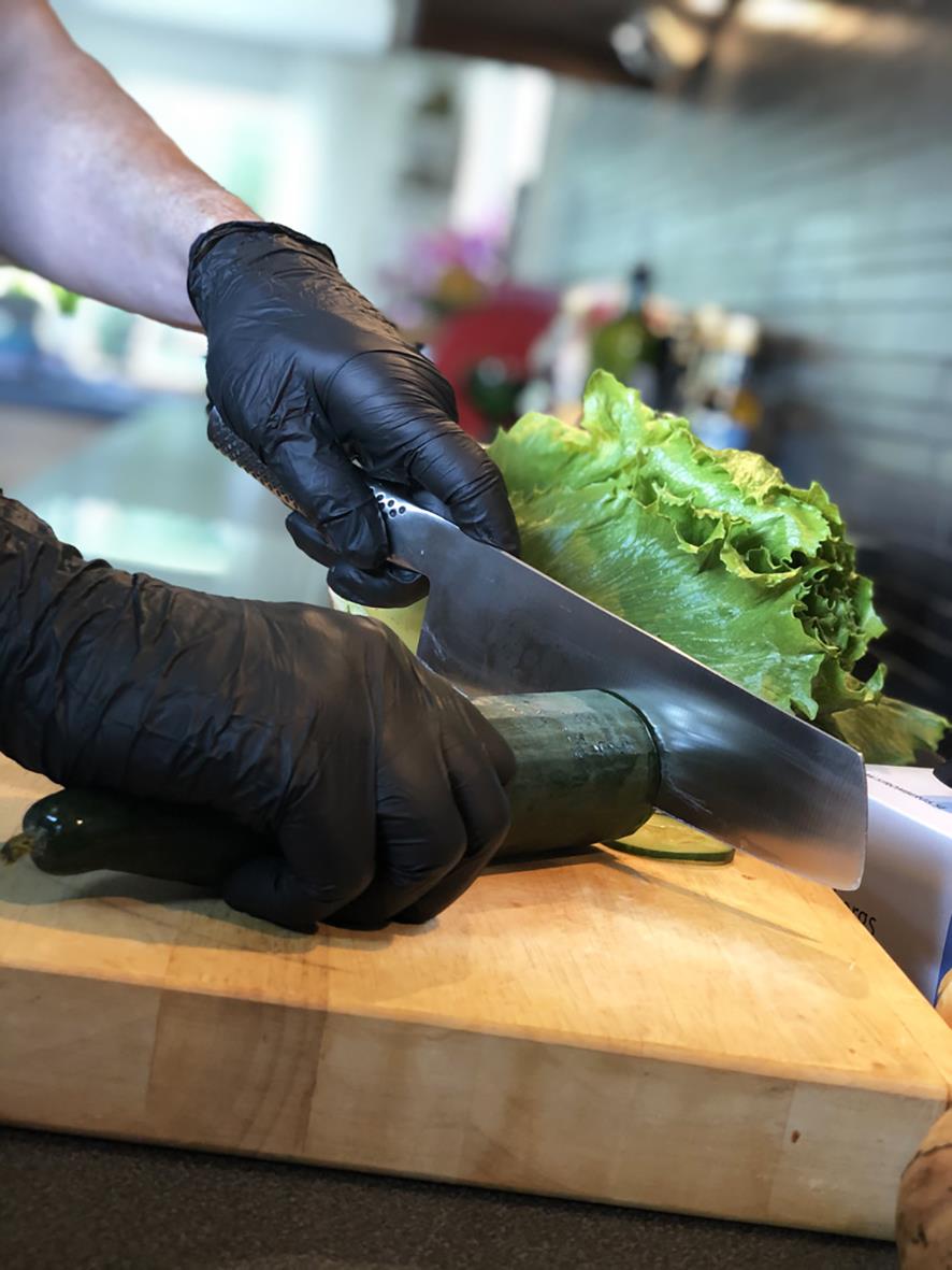 Person som skär grönsaker med svart nitrilhandske på i kök