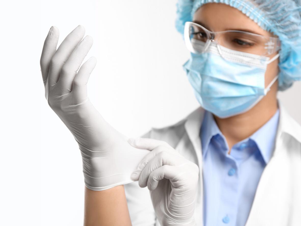 Person i skyddsutrustning som sätter på en vit nitrilhandske