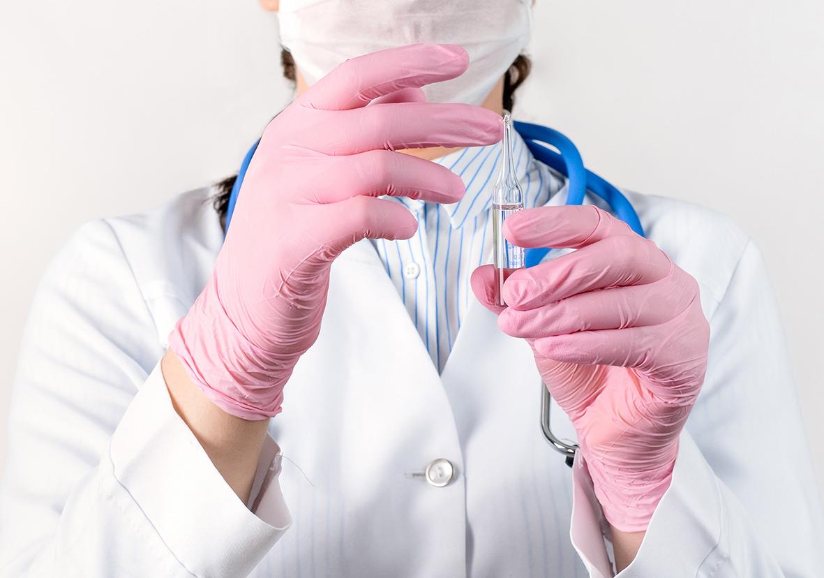 Person i vit labbrock och rosa nitrilhandskar hanterar ett provrör