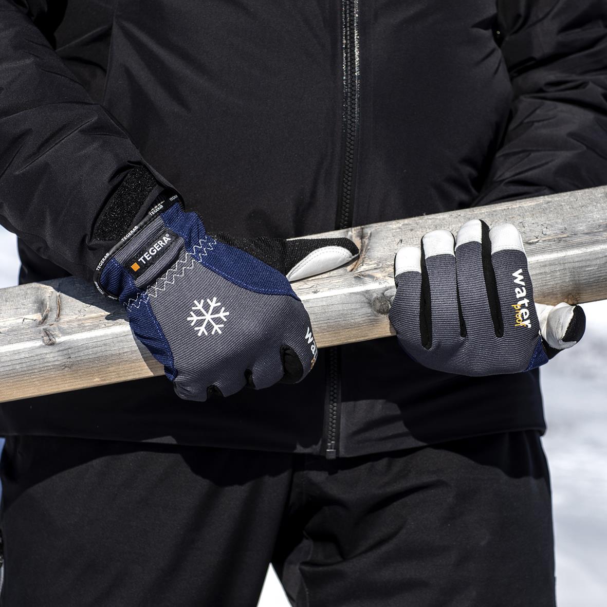 Person som bär Tegera 295 vinterhandske i blå och grå, vattentät, håller i en trästång