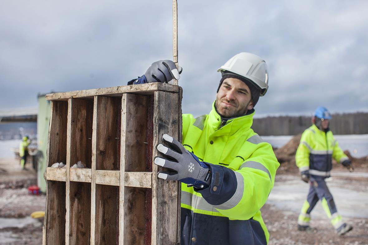 Arbetare i höga synliga kläder och hjälm som flyttar en träskiva på byggplats