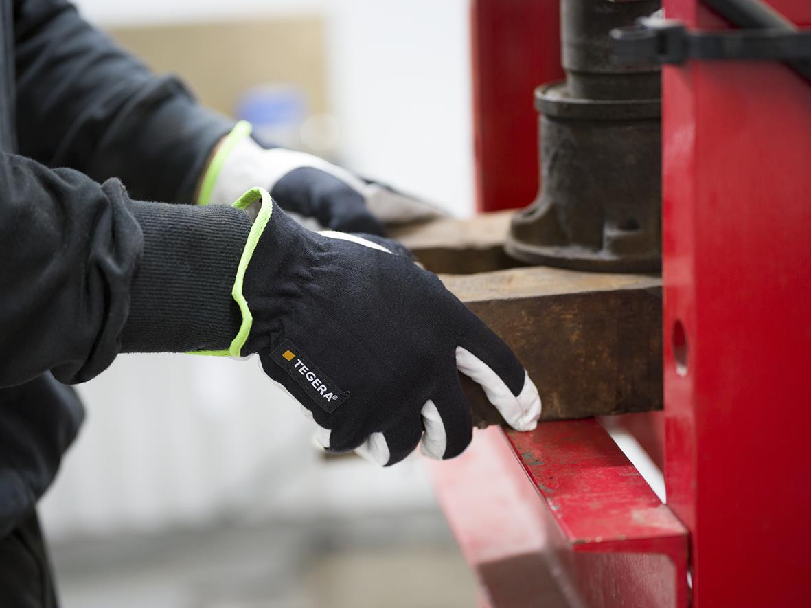 Person använder Tegera 511 läder monteringshandske för att hantera träbit i verkstadsmiljö