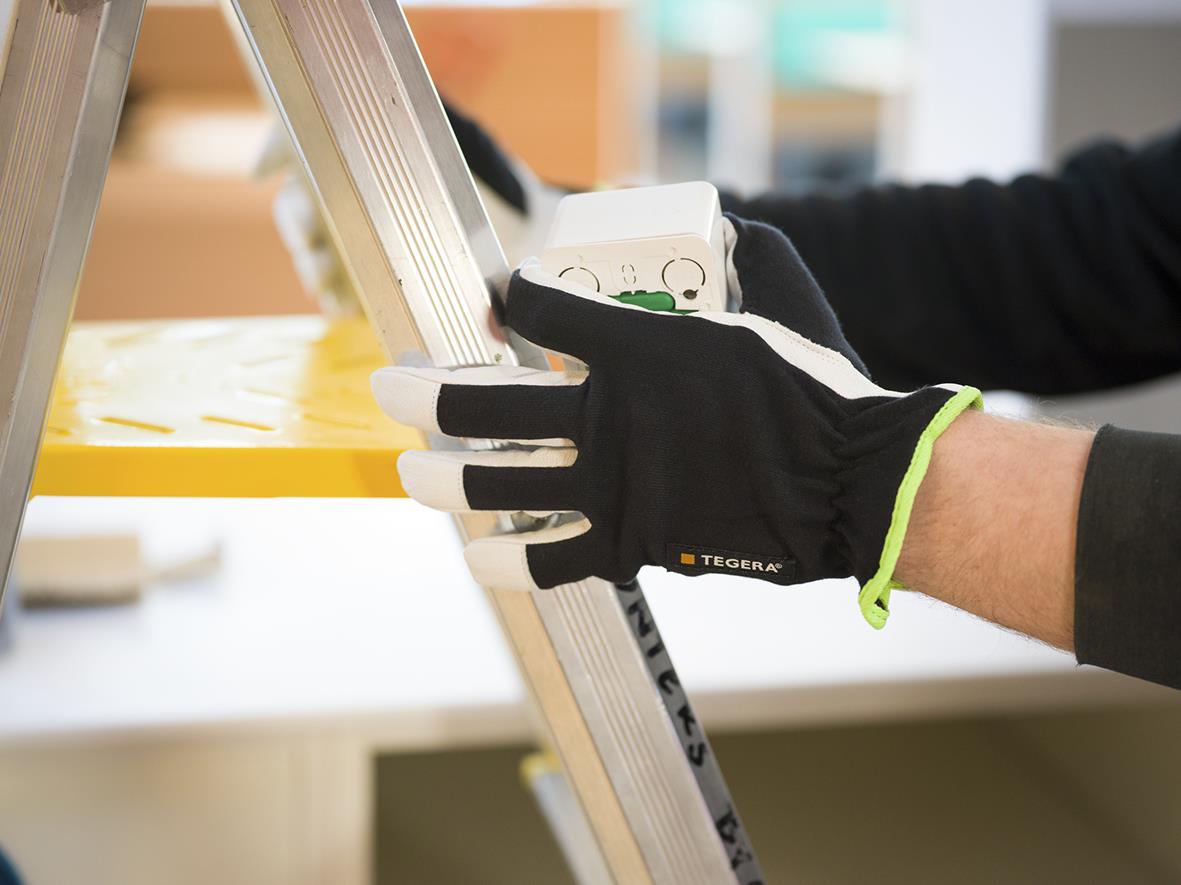 Person som använder Tegera 511 läder monteringshandske för att arbeta med en stege