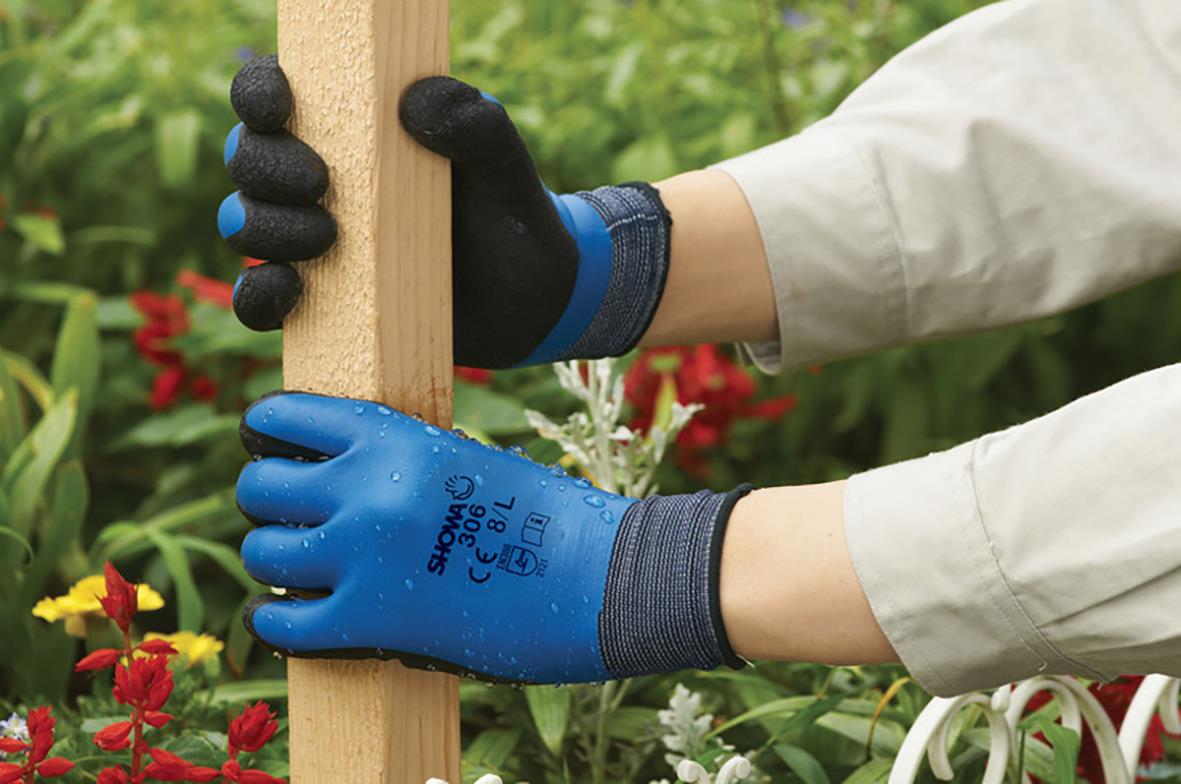 Person som arbetar med att mäta en trästolpe i en trädgård, bär blå och svarta latexhandskar