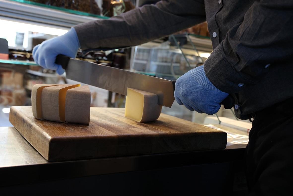 Person som skär i ost med skärskyddshandske Tegera 913 Blå på en köksbänk