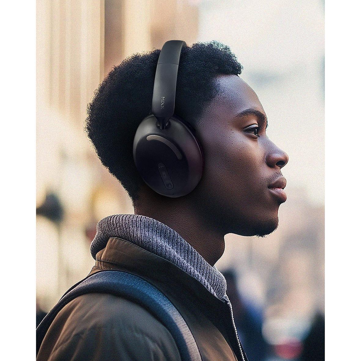 Ung man med svart hår bär trådlösa Mixx Over-Ear hörlurar i svart, utomhus