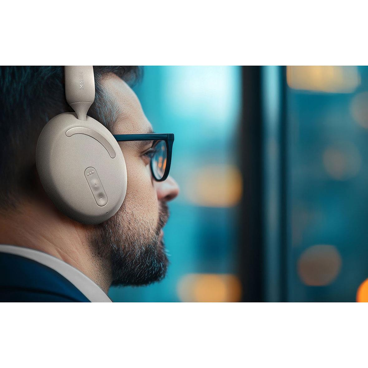 Man med svart hår och glasögon bär beige trådlösa hörlurar Mixx Over-Ear StreamQ D2 Sand