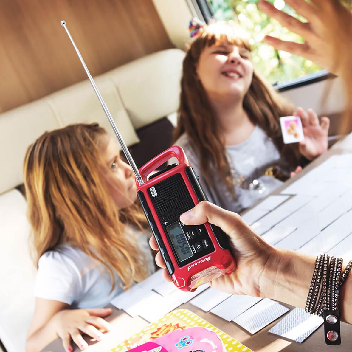 " barn leker med en nödradio och ficklampa/powerbank ER200 på ett bord, ett barn håller i radion medan ett annat tittar på."