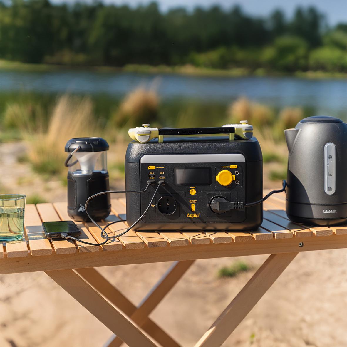 Portabel powerstation Aqiila Powebird S600V2 600W på träbord utomhus med vatten och natur i bakgrunden