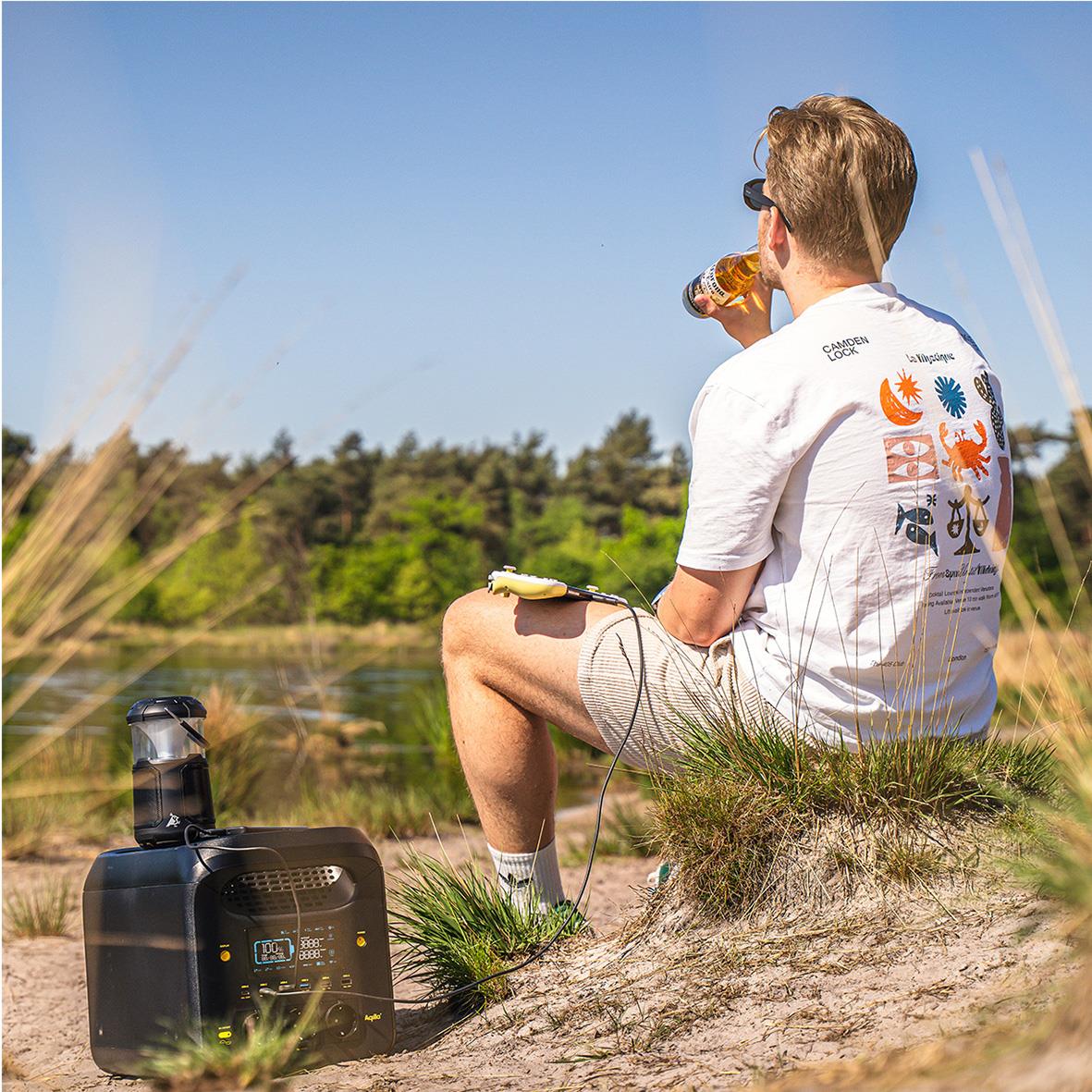 Man sitter vid sjö med Powerstation Aqiila Powebird S1800V2 1800W, dricker dryck och njuter av naturen