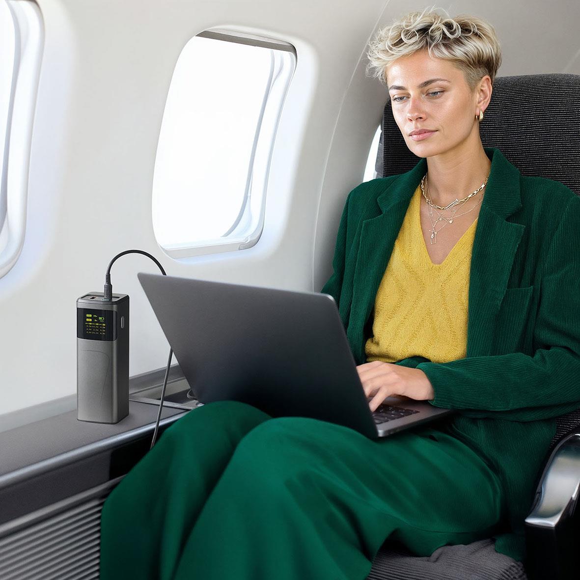 Kvinna arbetar på laptop ombord på ett flygplan med ett portabelt laddare bredvid sig