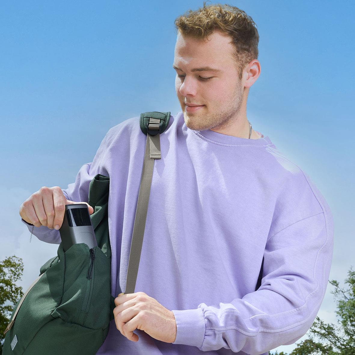 Ung man med ryggsäck som laddar sin powerbank utomhus mot en blå himmel