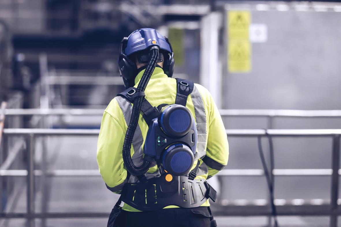 Person i skyddsutrustning med fläktpaket på ryggen i industriell miljö