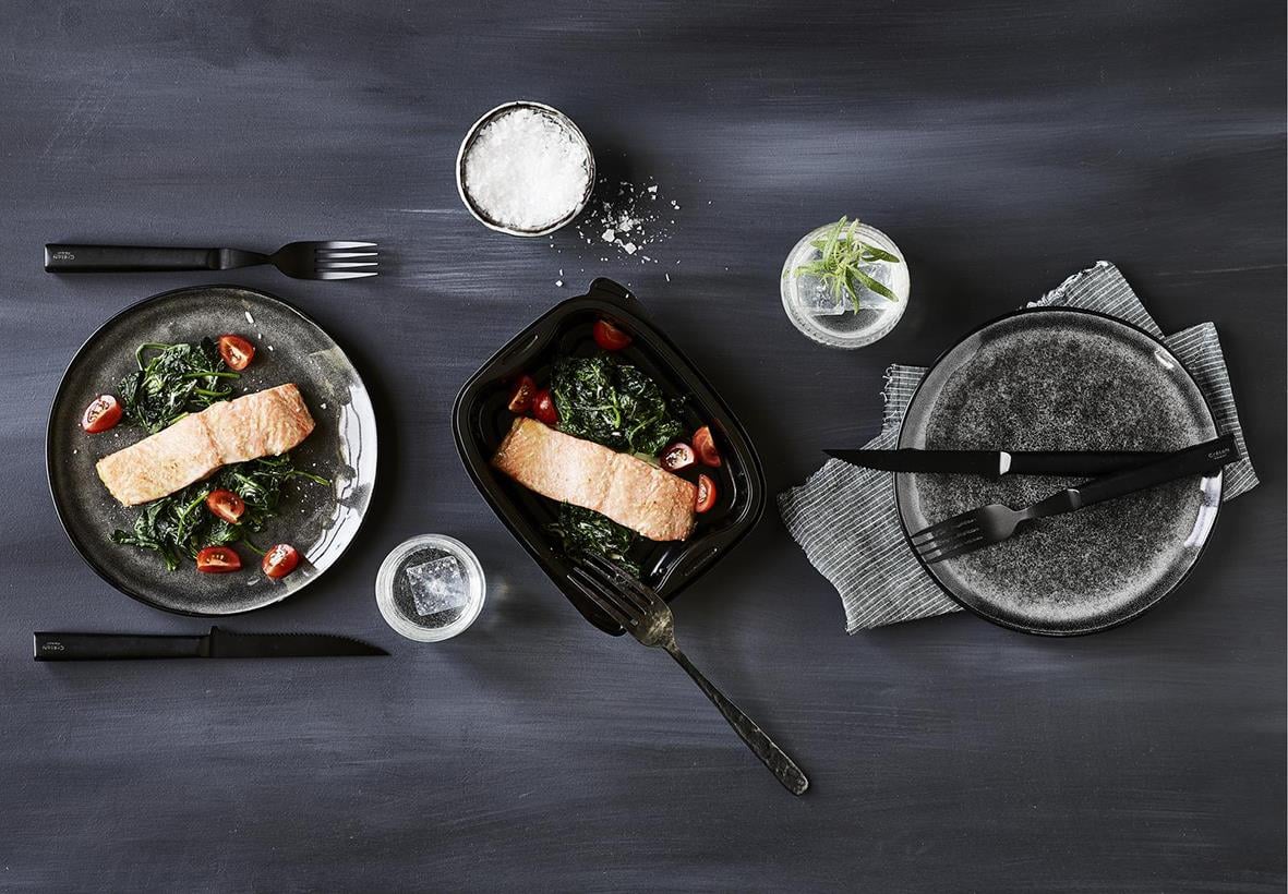 Plastform Bistro PP svart matlåda med lock, 190x155x41mm, 700ml, med tallrikar och bestick på mörk bakgrund