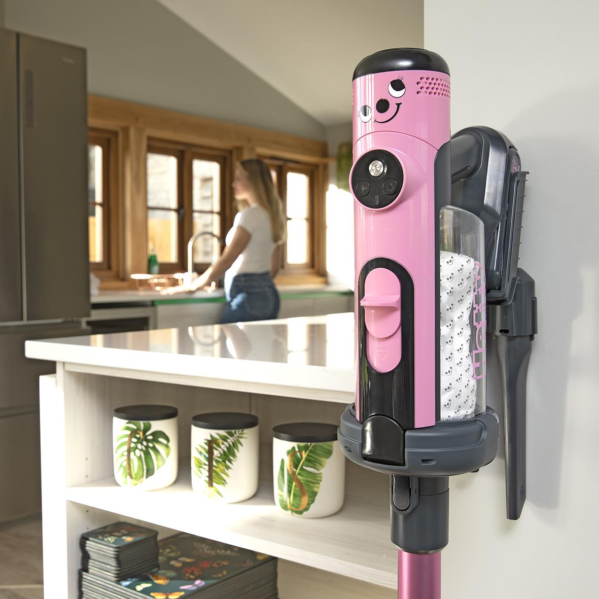 Dammsugare Numatic Henry Quick i röd med svart och rosa design står i ett hem, kök i bakgrunden med person vid diskbänk