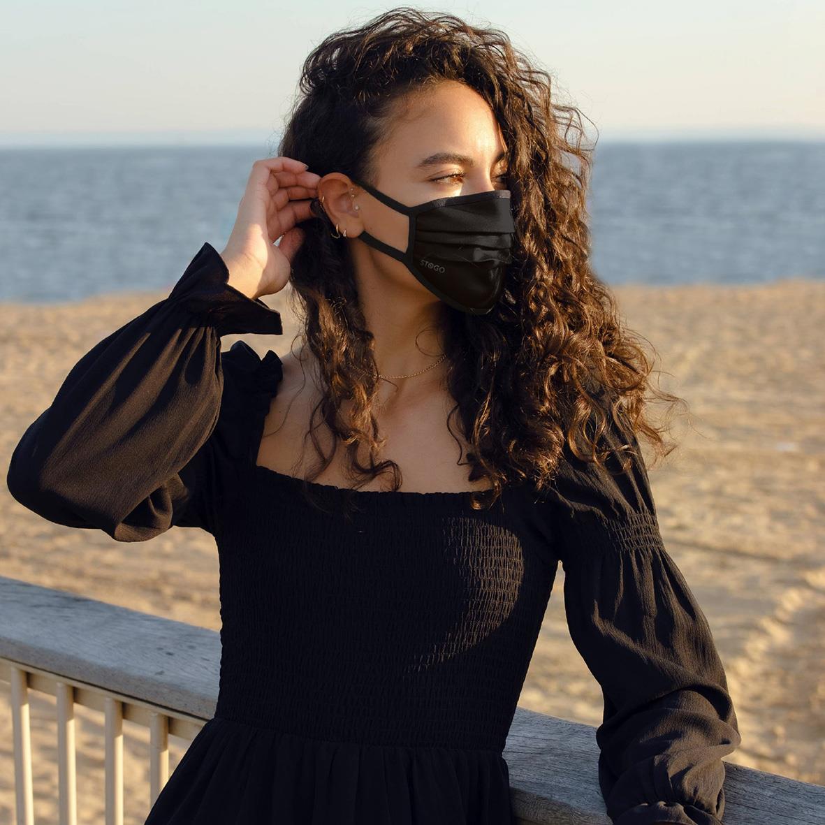 Kvinna med svart munskydd på strandpromenad, solnedgång i bakgrunden