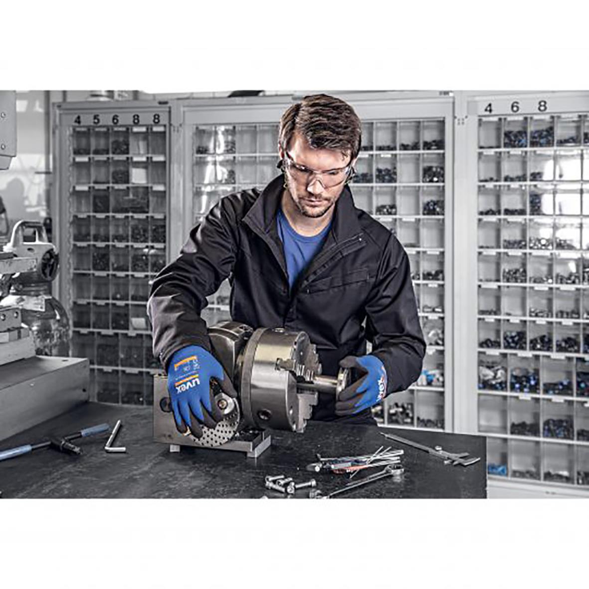 Man arbetar med metallverktyg i verkstad, bär Uvex Athletic Lite montagehandske och skyddsglasögon