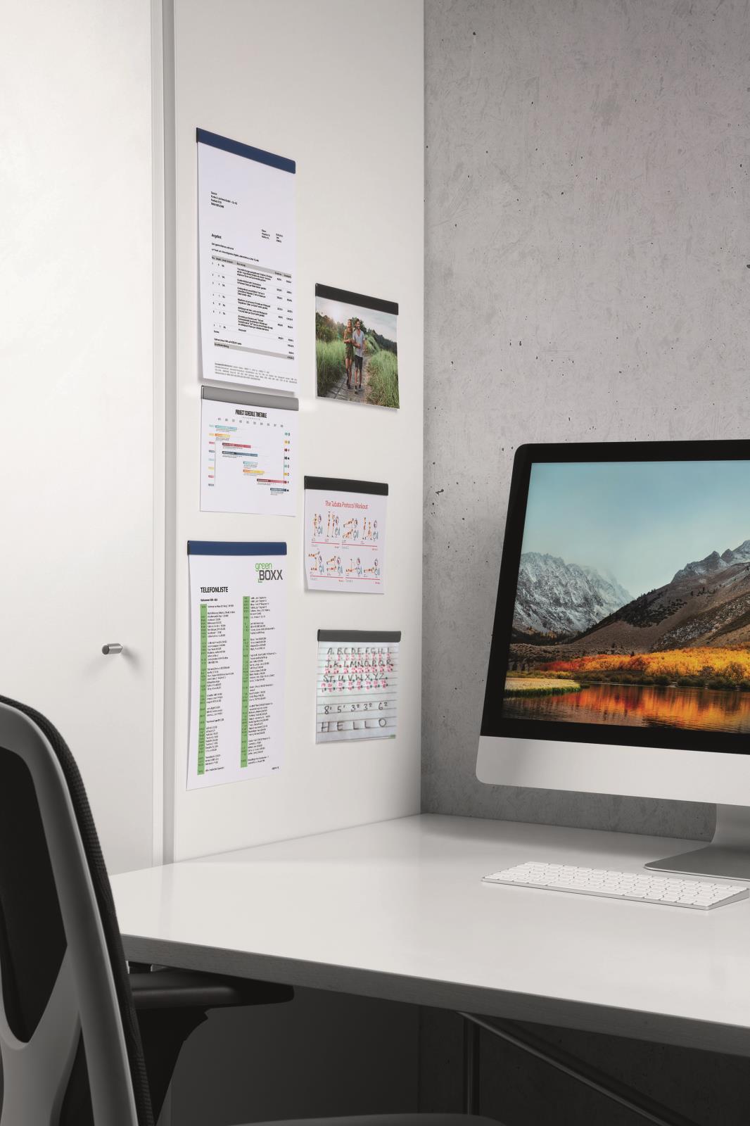 Vägg med olika dokument och bilder bredvid en dator på ett skrivbord