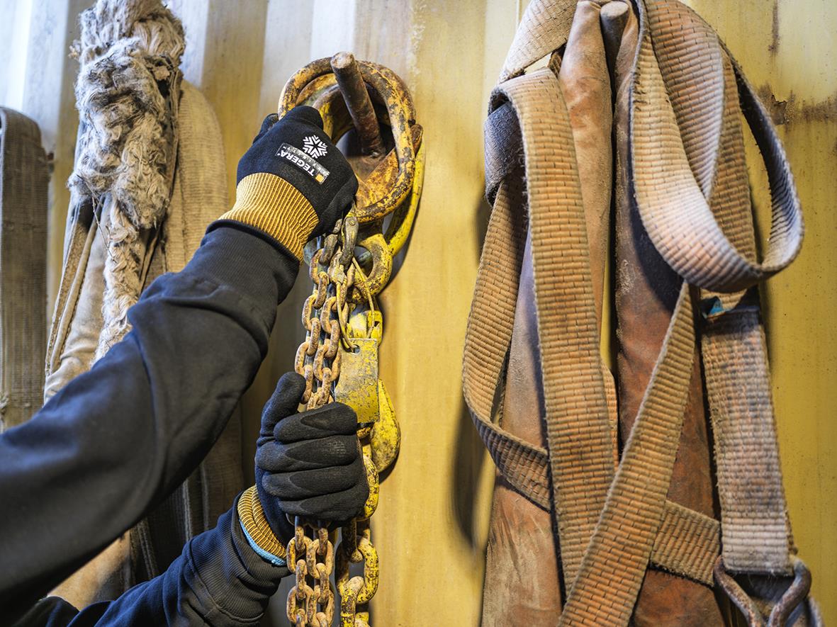 Person som håller i en kedja med montagehandske Tegera 8810R Infinity Nitrilfoam PU, omgivande arbetskläder